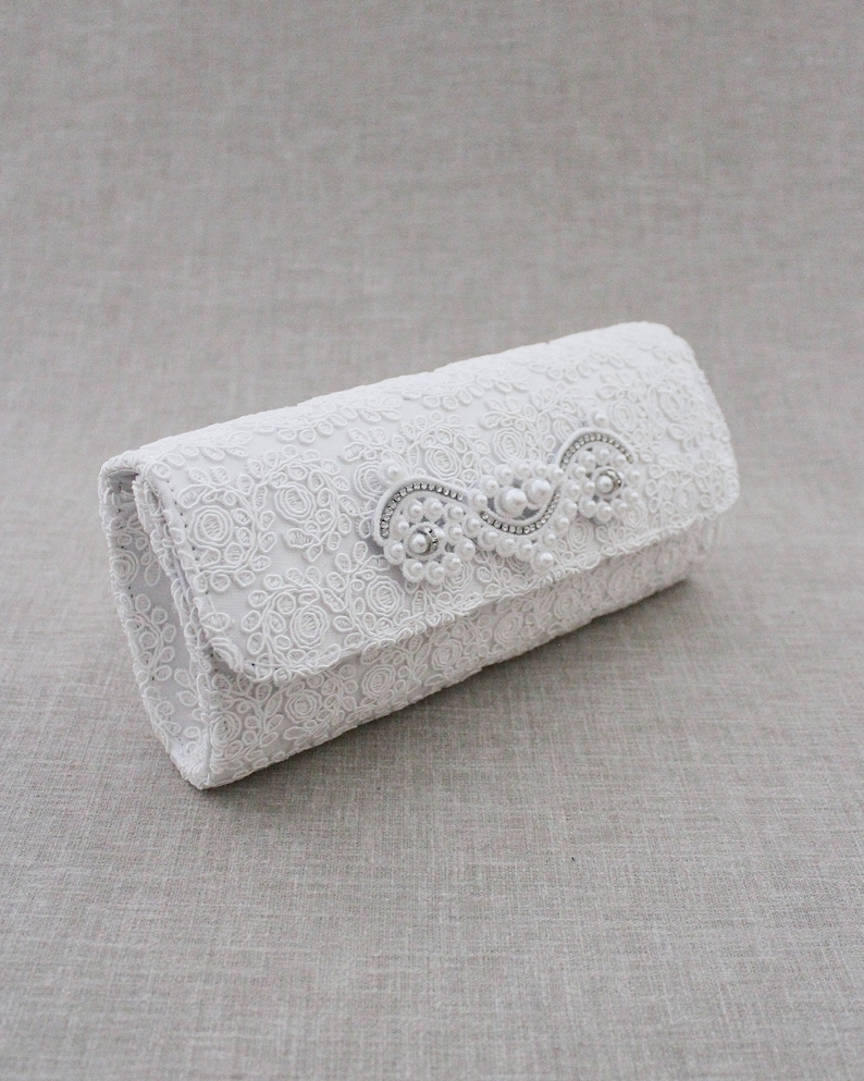 May include: White lace clutch with a pearl and rhinestone embellishment.