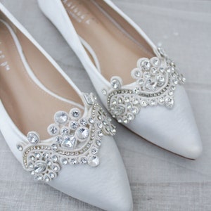 May include: Pair of white satin bridal shoes with pointed toes and jeweled embellishments.