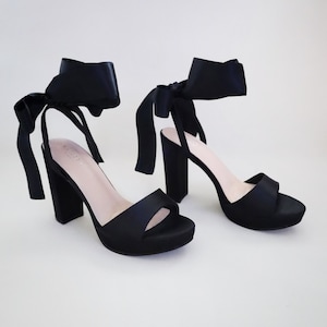 Könnte beinhalten: Schwarze Satin-Plateau-Heels mit einem dicken Blockabsatz und einem Satinband, das sich um den Knöchel bindet. Das Band ist oben am Knöchel zu einer Schleife gebunden.