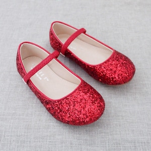 Puede incluir: Un par de bailarinas rojas de brillantina con una correa y cierre de hebilla. Los zapatos est&aacute;n hechos de un material suave y c&oacute;modo y tienen un acabado brillante.