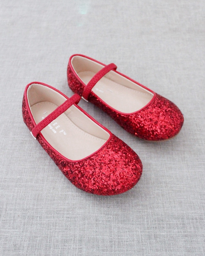Puede incluir: Un par de bailarinas rojas de brillantina con una correa y cierre de hebilla. Los zapatos est&aacute;n hechos de un material suave y c&oacute;modo y tienen un acabado brillante.