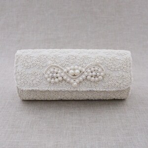 May include: A white clutch purse with a delicate floral lace design and a pearl embellishment.