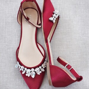 Puede incluir: Un par de zapatos planos de sat&eacute;n burdeos con adornos de cristal. Los zapatos de punta fina tienen correas en el tobillo con hebillas plateadas. Dise&ntilde;ados para una ocasi&oacute;n formal. Medidas en cent&iacute;metros.