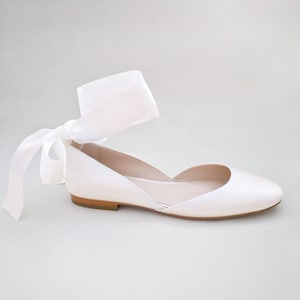May include: White satin flat shoes with a satin ribbon ankle tie. The ribbon is tied in a bow at the front of the shoe.