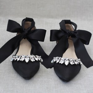 May include: Pair of black satin flats with a pointed toe and a large black satin bow on each shoe. The shoes are adorned with a row of clear rhinestones.