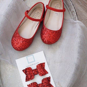 Puede incluir: Dos pares de lazos para el pelo de purpurina roja en una tarjeta blanca con el texto "KP www.kaileep.com". Los lazos est&aacute;n en una bandeja blanca con dos zapatos rojos de purpurina.