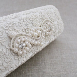 May include: White lace clutch with a pearl and rhinestone embellishment.