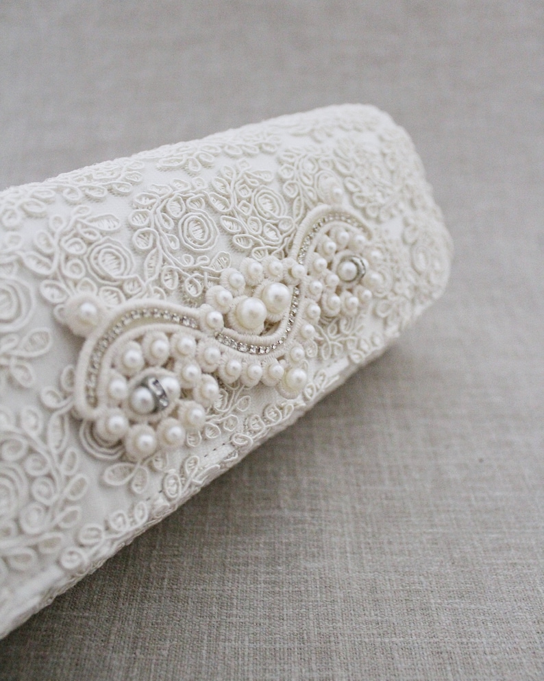 May include: White lace clutch with a pearl and rhinestone embellishment.