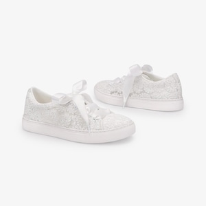 May include: A pair of white lace sneakers with white ribbon laces. The sneakers have a low profile, white rubber sole. The lace detailing covers the entire shoe, creating a delicate and elegant look. The sneakers are set against a plain white background.