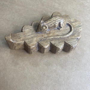 May include: A light brown wooden carving featuring a small mouse resting on top of a textured oak leaf. The piece displays a natural wood grain pattern throughout, with the mouse positioned centrally on the leaf and its long tail curved along the side.