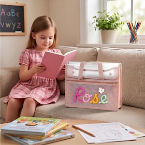 May include: A rectangular pink mesh storage bag with two top handles and a zipper closure. The front features the name Rose in colorful, textured, raised letters, accompanied by a small white flower applique. The bag is constructed from a semi-transparent mesh material with solid pink fabric trim and accents.