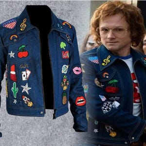 May include: A dark blue denim jacket featuring a variety of colourful embroidered patches including cherries, a rocket, a cactus, lips, a pineapple, a treble clef, stars, playing cards, and an American flag, with a pointed collar and front buttons.