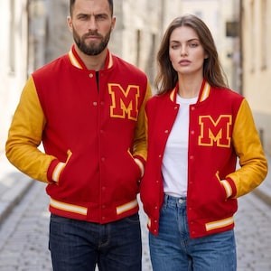 May include: A red varsity jacket with yellow sleeves, a ribbed collar, cuffs, and hem featuring white and yellow stripes. The jacket has a snap-button front closure and a large yellow letter M with a red outline on the left chest area.