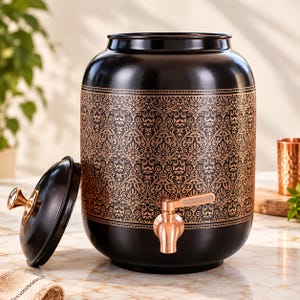 Könnte beinhalten: Ein schwarzer, zylindrischer Wasserspender mit einem breiten Band aus komplexen, kupferfarbenen Damastmustern in der Mitte. Er verfügt über einen passenden schwarzen Deckel mit Kupferknauf und einen kupferfarbenen Metallhahn an der Vorderseite.