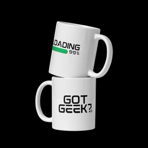 Puede incluir: Dos tazas de cerámica blanca apiladas verticalmente. La taza superior presenta el texto negro LOADING con una barra de progreso verde y 99% en negro. La taza inferior muestra el texto negro GOT GEEK? con un pequeño símbolo de marca registrada.