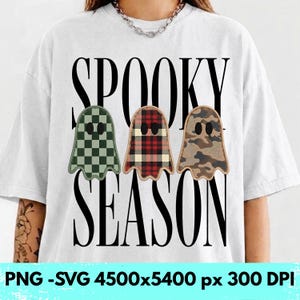 Op de afbeelding: Een wit t-shirt met de zwarte tekst SPOOKY SEASON en drie spookillustraties. Het eerste spook heeft een groen dambordpatroon, het tweede een rood en zwart ruitpatroon en het derde een bruin camouflagepatroon.