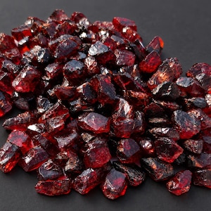 Peut inclure: Une collection de pierres précieuses grenat brutes d'un rouge profond, aux formes irrégulières et angulaires avec des surfaces facettées. Les pierres présentent divers niveaux de translucidité et des tons cramoisis saturés et sombres.