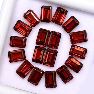 Peut inclure: Une collection de quinze pierres précieuses rectangulaires d'un rouge profond, facettées et disposées en cercle. Chaque pierre présente une taille émeraude classique avec des coins nets et des surfaces réfléchissantes sur fond blanc.