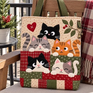 May include: A quilted tote bag featuring five appliquéd cats in various colors and patterns. The bag has olive green fabric handles, a red heart accent, and a small metal cat charm attached to a side loop. The base is a patchwork of red and green fabric.