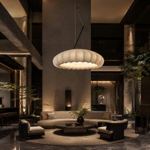 May include: A large, circular, off-white pendant light with a ribbed, cloud-like texture hangs from a thin black cord. The fixture emits a soft, diffused glow, illuminating the space below with a warm, even light that highlights its rounded form.
