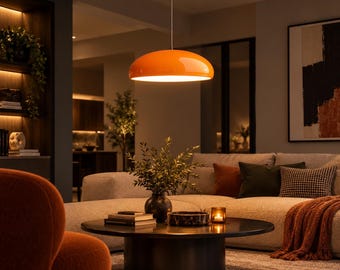 May include: A bright orange dome-shaped pendant light fitting suspended from the ceiling by a thin cord, featuring a smooth, glossy finish and a wide, circular shade that emits a warm, downward-facing glow over a living room space.