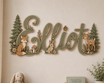 Può includere: Una targa da parete in legno con il nome Elliot in corsivo verde salvia, decorata con sagome sovrapposte di pini, una volpe, un coniglio, un cerbiatto, funghi e piccoli fiori nei toni della terra, marrone, crema e verde.