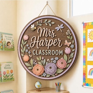 Pode incluir: Uma placa de parede redonda de madeira com o texto Mrs. Harper CLASSROOM em letras brancas. A placa &eacute; decorada com elementos florais 3D em tons de rosa, roxo e verde, juntamente com uma abelha, uma lib&eacute;lula e um detalhe de borboleta.