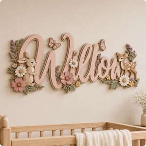 Pode incluir: Uma placa de madeira para parede com o nome Willow em letras cursivas grandes de cor rosa. O design é decorado com figuras tridimensionais de um coelho, um cervo, borboletas e várias flores em tons de rosa, branco e verde.