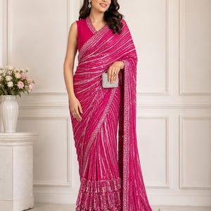 Puede incluir: Un sari fucsia vibrante con intrincados adornos de lentejuelas plateadas dispuestos en rayas verticales. La prenda incluye una blusa sin mangas con cuello en V y un drapeado fucsia a juego adornado con un borde decorativo y volantes escalonados.