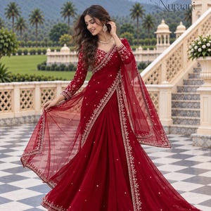 Può includere: Un sari rosso intenso con maniche lunghe e scollo a V, decorato con intricati ricami argentati lungo i bordi e motivi floreali sparsi. L'indumento include un dupatta rosso trasparente abbinato con un bordo ricamato in argento.