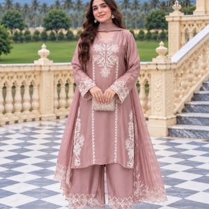 Könnte beinhalten: Ein altrosa dreiteiliges Outfit bestehend aus einer langärmeligen Tunika mit weißer Blumenstickerei, einer weiten Hose mit passender Saumstickerei und einem dazu passenden transparenten Dupatta, alles mit filigranen weißen Stickereien.