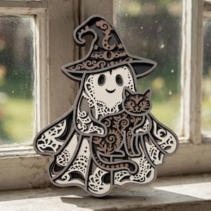 May include: A multi-layered wooden wall art piece featuring a ghost wearing a pointed hat and holding a cat. The design incorporates intricate laser-cut filigree patterns in shades of black, cream, and brown, creating a dimensional effect.