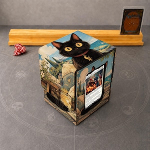 May include: A square deck box featuring a black cat illustration with yellow eyes and a crescent moon charm on its collar. The box displays a landscape scene and holds a single trading card in a clear front window slot.