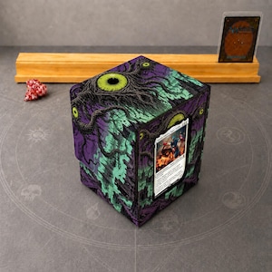 May include: A square trading card deck box featuring a purple and green graphic of a large eye with dark roots. A Captain America Super Soldier card is displayed in a clear front window. A red multi-sided die sits nearby.