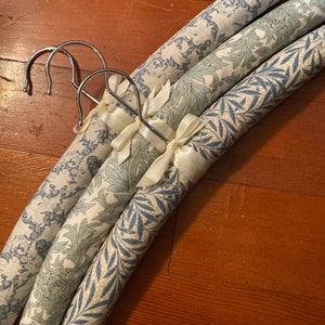 May include: Three padded hangers with blue and white floral patterns. The hangers are made of metal and have a satin ribbon tied around the top.