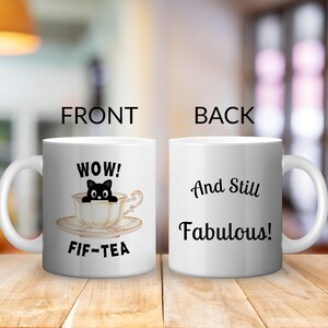 May include: A white ceramic mug shown from two angles. The front features a black cat peeking out of a teacup with the text "WOW! FIF-TEA". The back displays the text "And Still Fabulous!" in black script and print lettering on the white surface.