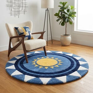 May include: A round area rug featuring a central yellow sun motif surrounded by concentric blue circles and a border of white triangles. The rug is placed on a wooden floor in front of an armchair with a blue and yellow patterned pillow.