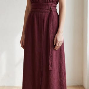 May include: A deep burgundy midi-length dress featuring a V-neckline, cap sleeves, and a matching fabric belt with a D-ring buckle at the waist. The garment has a straight skirt silhouette with a vertical seam down the center front.