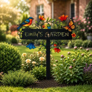 May include: A black metal garden sign on a stake featuring the text "Emily's Garden" in gold lettering. The sign is decorated with a colorful blue and orange bird, a monarch butterfly, and various painted flowers and green vines.