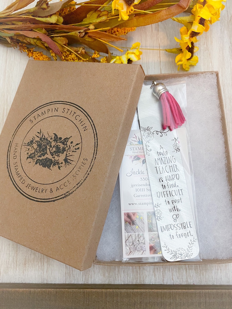 May include: A silver bookmark with a pink tassel. The bookmark has a floral design and the text "A truly amazing teacher is hard to find, difficult to part with, & impossible to forget."