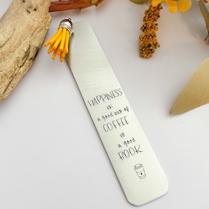 May include: A silver metal bookmark with the text "HAPPINESS is: a good cup of COFFEE and a good BOOK." The bookmark has a yellow tassel attached to the top. A small coffee cup graphic is at the bottom.