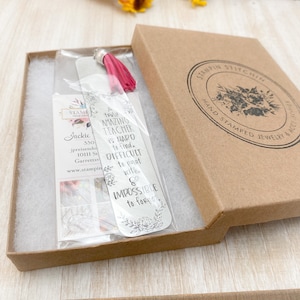 May include: A silver bookmark with a pink tassel, packaged in a brown box. The bookmark has a quote that reads "A truly amazing teacher is hard to find. Difficult to part with. & Impossible to forget."