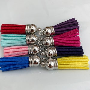 Op de afbeelding: Een set van zeven kleurrijke kwastjes met zilveren metalen dopjes. De kwastjes zijn in de kleuren rood, turquoise, roze, blauw, marine, geel en paars.