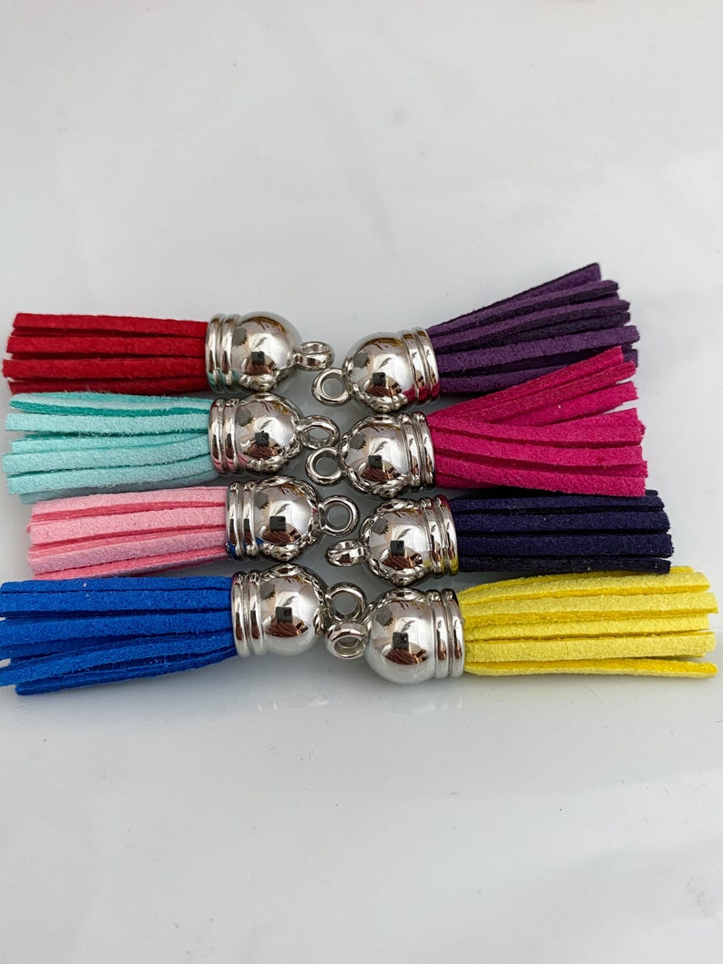 Op de afbeelding: Een set van zeven kleurrijke kwastjes met zilveren metalen dopjes. De kwastjes zijn in de kleuren rood, turquoise, roze, blauw, marine, geel en paars.