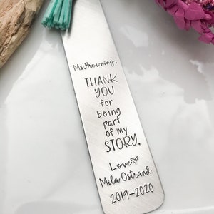 May include: A silver bookmark with a turquoise tassel. The bookmark has the text "Ms. Browning, THANK YOU for being part of my STORY. Love Mila Ostrand 2019-2020" engraved on it.