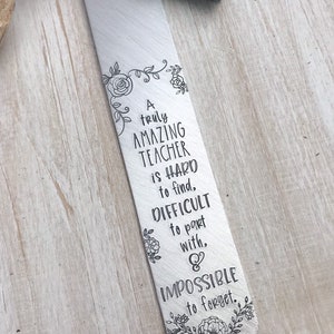 Op de afbeelding: Een zilveren metalen bladwijzer met een turquoise kwast. De bladwijzer heeft een bloemmotief en de tekst "A truly AMAZING TEACHER is HARD to find, DIFFICULT to part with, & IMPOSSIBLE to forget."