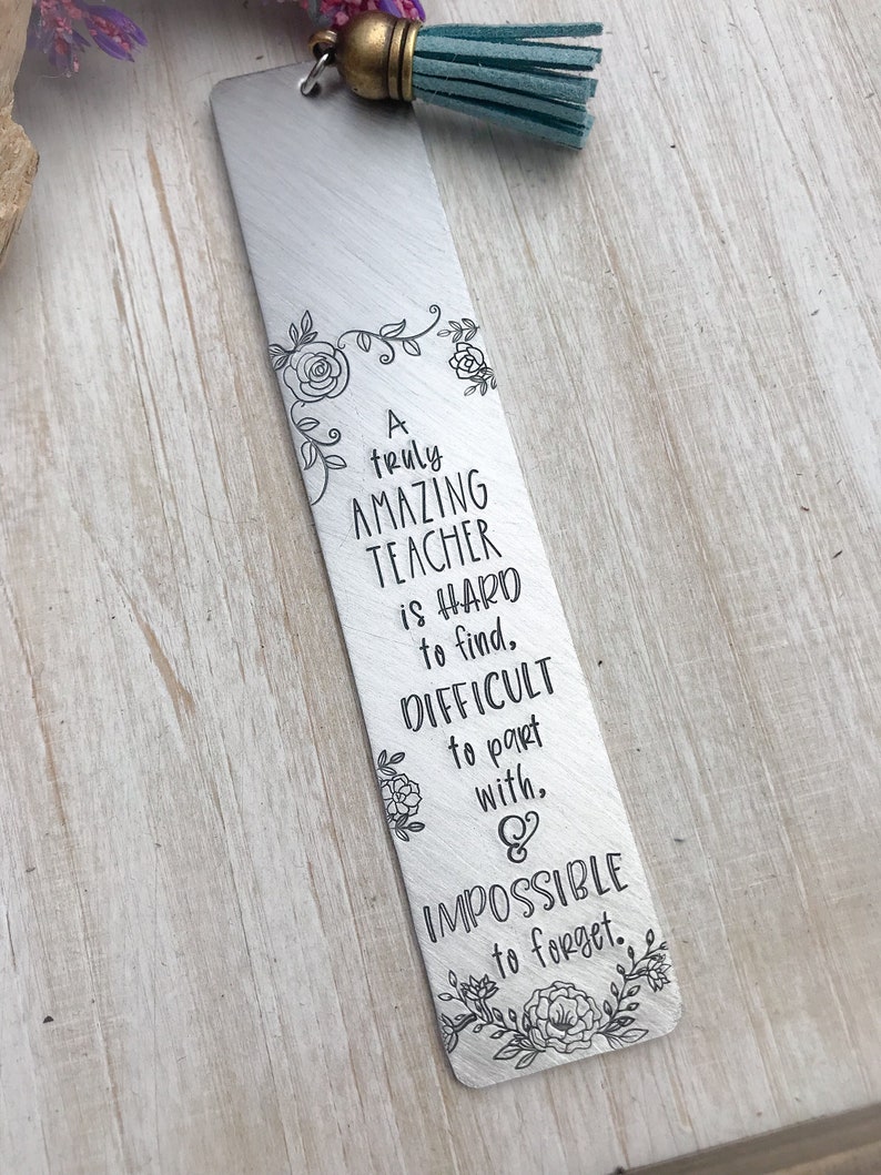 May include: A silver bookmark with a teal tassel. The bookmark features a floral design and the text "A truly AMAZING TEACHER is HARD to find, DIFFICULT to part with, & IMPOSSIBLE to forget."