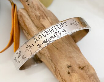 Könnte beinhalten: Silberarmband mit gehämmerter Oberfläche und der Inschrift "Adventure awaits" mit einem Pfeil, der nach rechts zeigt. Das Armband hat außerdem eine Kompassrose und Pfeile.