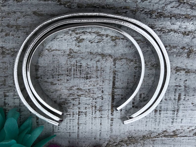 May include: Two silver metal bracelets stacked on top of each other. The bracelets are round and have a smooth, polished finish.