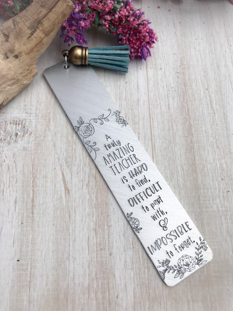 Op de afbeelding: Een zilveren bladwijzer met een turquoise kwast. De bladwijzer heeft een bloemmotief en de tekst "A truly AMAZING TEACHER is HARD to find, DIFFICULT to part with, & IMPOSSIBLE to forget."